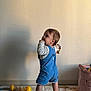 toddler, child, blue_overalls, toy, play_mat, barefoot, indoor, shadow, wall, curious, standing, baby, floor, colorful_toy, long_sleeve_shirt, young_child, person, home, cute, playtime