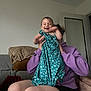 baby, child, adult, laughing, smiling, dress, purple_hoodie, couch, blanket, living_room, indoor, person, happy, playful, seated, holding, joy, casual, home, fun