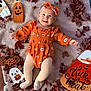 baby, infant, orange_clothing, headband, smiling, blanket, autumn_leaves, halloween, pumpkin, ghost, decorations, milestone_sign, tights, cute, festive, holiday, lying_down, indoor, seasonal, person
