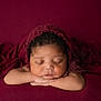 arms, baby, burgundy, child, closeup, curly_hair, cute, fabric, headwear, indoors, infant, knitted_bonnet, newborn, peaceful, portrait, relaxed, resting, skin, sleeping, soft_lighting