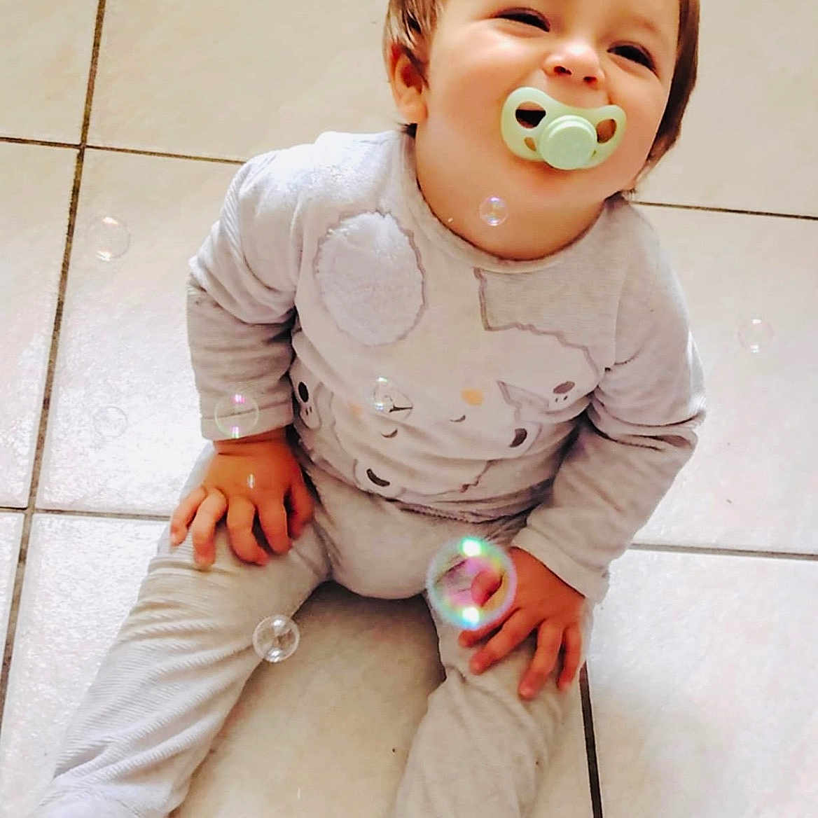 Ezio participe au concours pour gagner de l'argent avec cette photo : baby, bubbles, child, clothing, cute, feet, floor, hair, hands, happy, indoors, infant, onesie, pacifier, playful, sitting, skin, smile, tile, young