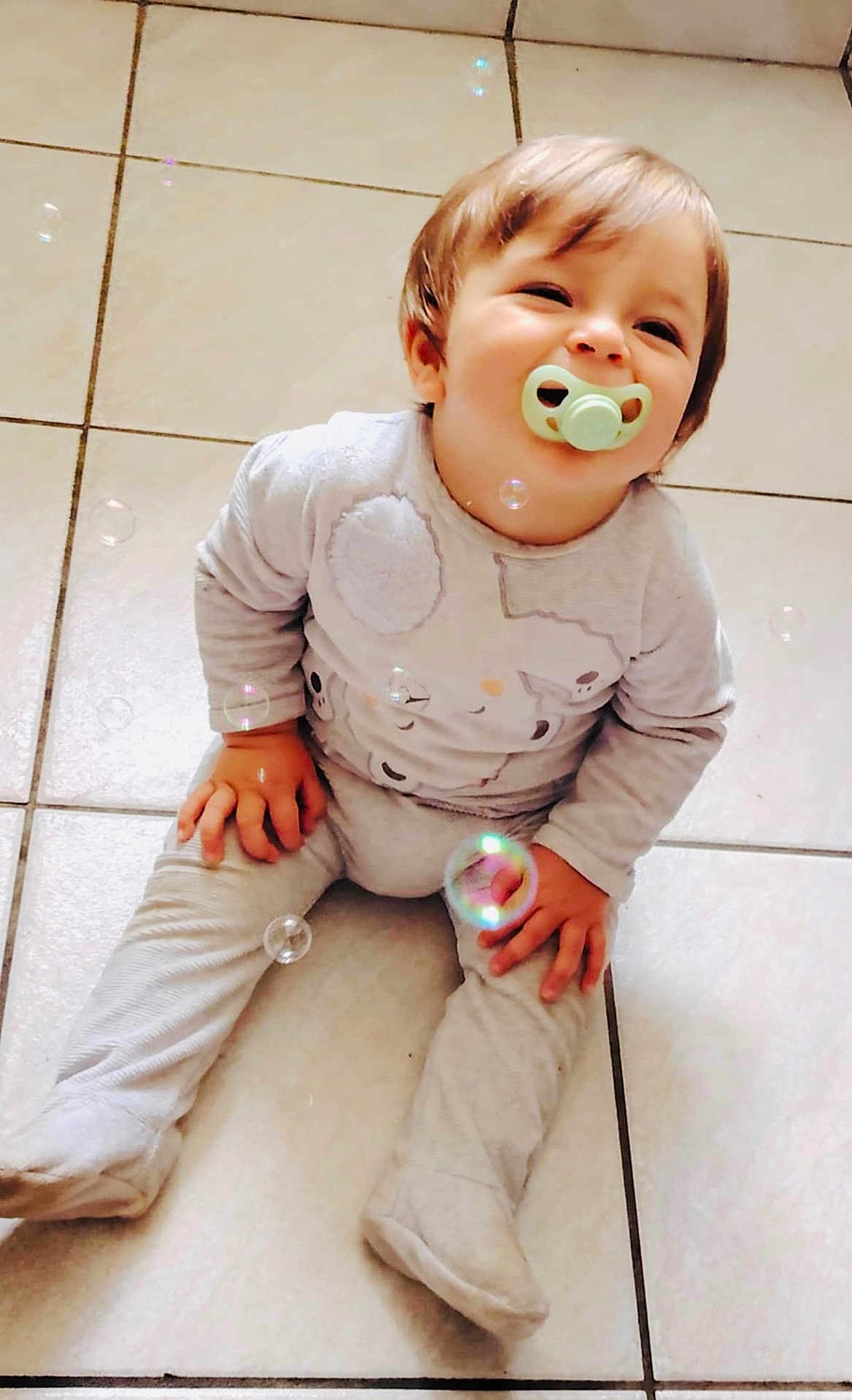 Ezio participe au concours pour gagner de l'argent avec cette photo : baby, child, pacifier, sitting, floor, tile, bubbles, happy, clothing, onesie, infant, cute, smile, indoors, playful, hands, feet, hair, skin, young