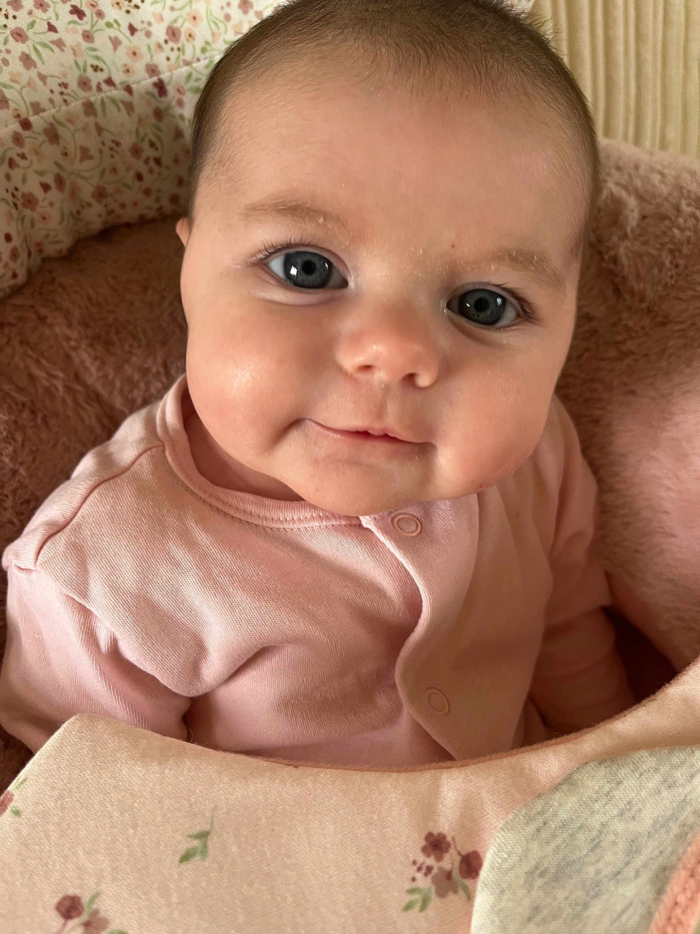 Talia is registered to the contest to win money with this photo: baby, infant, face, eyes, smile, pink_clothing, blanket, plush, soft, cute, child, portrait, indoor, young, skin, head, sitting, cozy, closeup, adorable