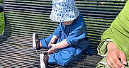 Huraira Muhammad joined the competition — help win amazing prizes! toddler, child, bench, outdoor, sunlight, blue_clothing, hat, shoe, tying_shoes, adult, green_clothing, hand, grass, metal_bench, casual, daytime, sitting, focus, park, person