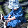 toddler, child, bench, outdoor, sunlight, blue_clothing, hat, shoe, tying_shoes, adult, green_clothing, hand, grass, metal_bench, casual, daytime, sitting, focus, park, person