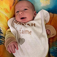 Léo a rejoint le concours — aidez-le/la à gagner de superbes lots ! baby, infant, blanket, bib, yellow_clothing, face, hand, portrait, cute, child, newborn, soft_texture, sleepwear, lying_down, closeup, smile, indoor, warm_colors, cozy, expression