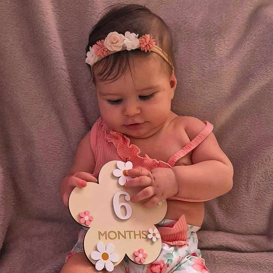 Louna participe au concours pour gagner de l'argent avec cette photo : 6_months, adorable, baby, child, cute, decorative_sign, floral_pattern, flower_headband, girl, hands, headband, holding_sign, indoor, infant, looking_down, pink_clothing, portrait, sitting, soft_blanket, young_child