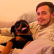 Archie is registered to the contest to win money with this photo: dog, rottweiler, man, smiling, couch, blanket, indoor, cozy, pet, friendship, relaxing, comfort, casual, portrait, happy, living_room, furniture, people, animal, home