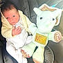 newborn, baby, infant, crocheted_toy, dinosaur, stuffed_animal, white_onesie, cream_sweater, cushion, car_seat, child, cute, soft_toy, handmade, knitted, portrait, indoor, cozy, person, baby_clothing