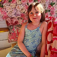 Mélina a rejoint le concours — aidez-le/la à gagner de superbes lots ! child, girl, freckles, smile, blue_dress, couch, pillow, blanket, flower_wall, roses, indoor, portrait, relaxed, sunlight, skin, hair, hand, cozy, decor, seated