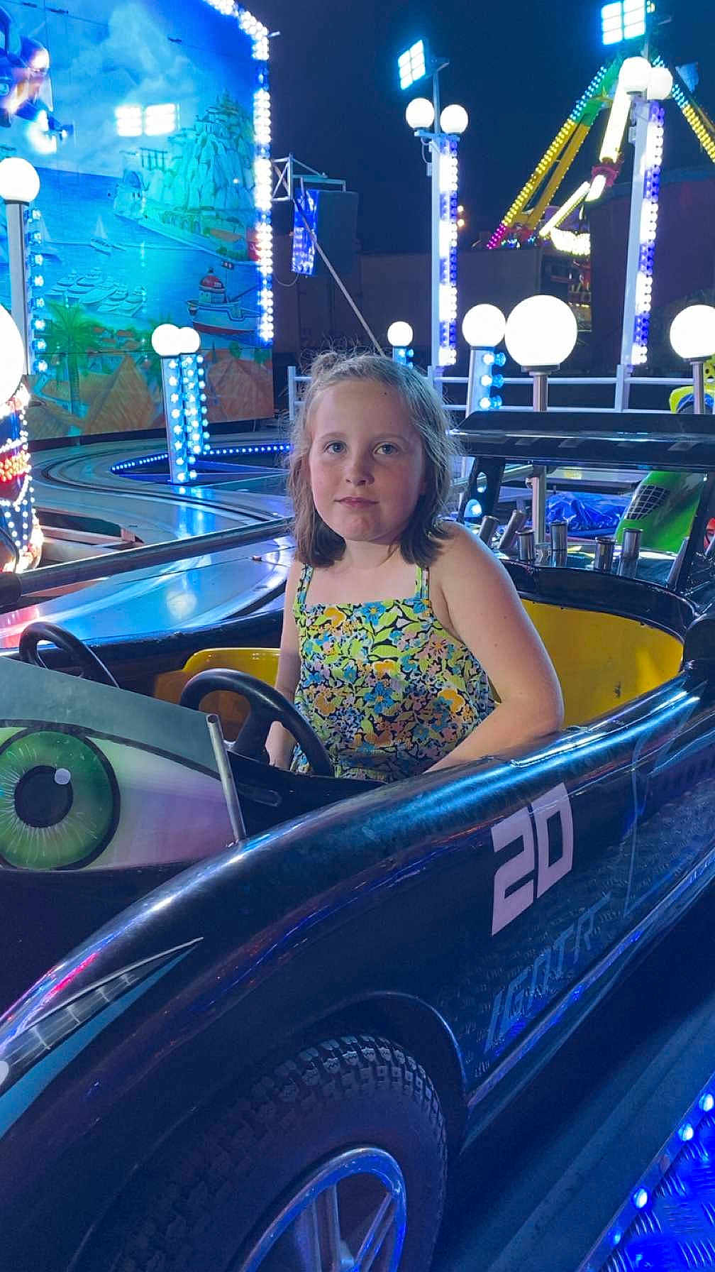 Mélina a rejoint le concours — aidez-le/la à gagner de superbes lots ! child, girl, bumper_car, amusement_park, night, lights, ride, vehicle, fun, entertainment, young, person, casual_clothing, blue_lights, colorful, outdoor, seat, steering_wheel, smile, portrait