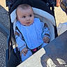 baby, stroller, bib, outdoor, child, table, shadow, clothing, infant, face, seat, person, curious, sunlight, pavement, hands, jacket, expression, young, cute