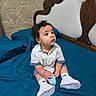 Enzo joined the competition — help win amazing prizes! baby, child, infant, sitting, bed, bedroom, blue_bedding, white_shoes, sneakers, curly_hair, portrait, looking_away, curious, clothing, shirt, shorts, indoors, wooden_headboard, stone_wall, photography