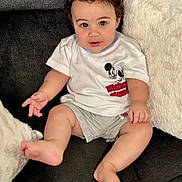 Enzo is registered to the contest to win money with this photo: baby, child, infant, sitting, sofa, couch, pillow, white_pillow, curly_hair, smiling, facial_expression, portrait, indoor, home, clothing, mickey_mouse, t_shirt, barefoot, legs, photography