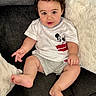 baby, child, infant, sitting, sofa, couch, pillow, white_pillow, curly_hair, smiling, facial_expression, portrait, indoor, home, clothing, mickey_mouse, t_shirt, barefoot, legs, photography