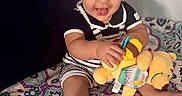 Enzo joined the competition — help win amazing prizes! baby, child, toddler, smiling, sitting, stuffed_animal, toy, plush_toy, teething_ring, bed, bedspread, patterned_fabric, indoors, portrait, curly_hair, striped_clothing, infant, playtime, happy, feet