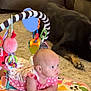 baby, infant, play_mat, toy, dog, carpet, living_room, couch, pink_clothing, polka_dots, floor, pet, animal, child, cute, indoors, resting, colorful, curious, soft_lighting