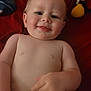 baby, child, smiling, bare_chest, pointing, plush_toy, red_blanket, lying_down, infant, cute, happy, skin, hand, face, portrait, indoors, young_child, expression, soft_toy, comfort