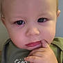 baby, blonde_hair, casual_clothing, child, close_up, curious, cute, expression, face, finger_in_mouth, green_shirt, hand, indoors, pensive, person, portrait, skin, text_on_clothing, toddler, young_child