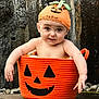 baby, basket, child, costume, cute, decoration, expression, face, festive, halloween, hat, holiday, infant, orange, outdoor, pumpkin, rock, sitting, small, smile