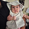 Astrid is registered to the contest to win money with this photo: baby, bodypart, bonnet, cap, clothing, couch, diaper, dress, face, finger, furniture, hand, hat, head, hood, person, photography, portrait, sitting, sunhat