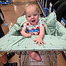 Emilio is registered to the contest to win money with this photo: baby, shopping_cart, store, aisle, tire, floor, footwear, person, clothing, hand, foot, cover, pattern, happy, child, indoor, sitting, retail, curious, smiling