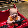 Emilio joined the competition — help win amazing prizes! baby, child, smiling, shopping_cart, toy_car, red, grocery_store, bread, shelf, floor, happy, steering_wheel, infant, clothing, orange_shirt, retail, store, supermarket, person, indoor