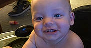 Emilio joined the competition — help win amazing prizes! baby, child, face, smile, food, indoor, highchair, furniture, shoe, carpet, person, mess, hand, head, cheek, eyes, mouth, skin, expression, table