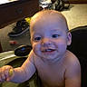 baby, child, face, smile, food, indoor, highchair, furniture, shoe, carpet, person, mess, hand, head, cheek, eyes, mouth, skin, expression, table