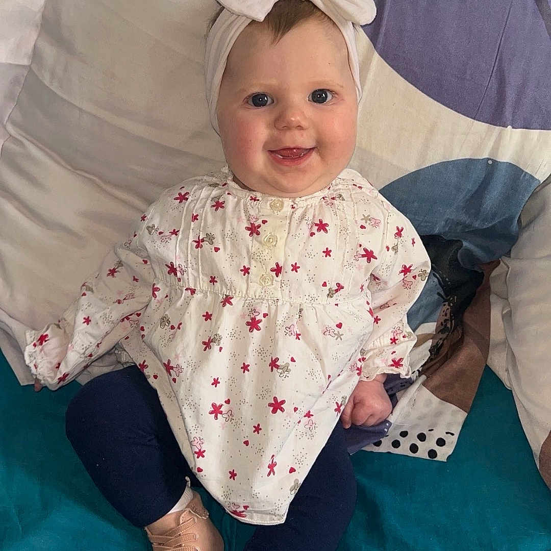 Leïya a rejoint le concours — aidez-le/la à gagner de superbes lots ! baby, bed, blanket, bow, child, clothing, cute, flower_print, happy, headband, indoors, infant, leggings, long_sleeve, person, pillow, portrait, shoes, sitting, smiling