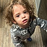 blue_shoes, casual_wear, child, clothing, curly_hair, expression, fleece_jacket, flooring, holding_hand, home, indoor, looking_up, panda_pattern, person, standing, striped_skirt, support, toddler, wood_floor, young_child