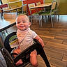 baby, child, infant, smiling, happy, portrait, high_chair, restaurant, dining_area, indoor, seated, bib, pink_clothing, barefoot, wooden_floor, tables, chairs, cafeteria, daylight, photography