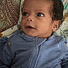 Noah is registered to the contest to win money with this photo: baby, child, infant, portrait, close_up, curly_hair, wide_eyes, looking_away, blue_clothing, pajamas, lying_down, bed, bedding, blanket, patterned_background, home, indoors, face, cozy, photograph
