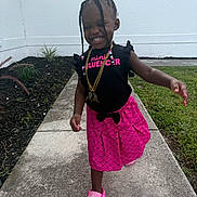 Miliana is registered to the contest to win money with this photo: child, girl, smiling, braids, pink_skirt, black_top, outdoor, sidewalk, grass, garden, happy, walking, footwear, accessories, necklace, hair_bun, casual_clothing, daylight, portrait, cute