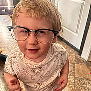 Tatum is registered to the contest to win money with this photo: child, glasses, shirt, cartoon, indoor, floor, tile, curly_hair, playful, person, young_child, smiling, casual_clothing, home, background, door, light, standing, cute, portrait
