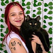 Simon joined the competition — help win amazing prizes! woman, pink_hair, black_cat, cat, tattoo, smiling, portrait, indoor, leaf_pattern, green_leaves, white_shirt, happy, pet, holding, animal, cute, face, long_hair, yellow_eyes, feline