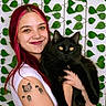 woman, pink_hair, black_cat, cat, tattoo, smiling, portrait, indoor, leaf_pattern, green_leaves, white_shirt, happy, pet, holding, animal, cute, face, long_hair, yellow_eyes, feline