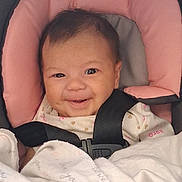Kaylani is registered to the contest to win money with this photo: baby, smiling, car_seat, blanket, infant, seatbelt, pink, gray, clothing, face, cute, child, happy, portrait, indoor, person, newborn, head, sitting, baby_girl