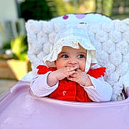 Esmée participe au concours pour gagner de l'argent avec cette photo : baby, child, high_chair, hat, red_clothing, white_hat, cute, infant, fingers_in_mouth, knitted_blanket, outdoor, daylight, portrait, happy, smiling, seat, young_child, face, person, baby_girl
