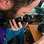 person, kitten, black_cat, holding, indoor, close_up, affection, beard, hand, furniture, table, carpet, jeans, purple_shirt, face, pet, cute, animal, love, home
