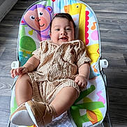 Narel joined the competition — help win amazing prizes! baby, child, infant, smiling, happy, portrait, seated, bouncer, activity_seat, knitted_outfit, beige_clothing, shoes, colorful_cushion, indoor, wood_floor, home, natural_light, face, playful, adorable