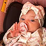 adorable, baby, blanket, bow, car_seat, close_up, cozy, eyes, floral_clothing, hand, headband, infant, newborn, pacifier, pacifier_clip, pink, portrait, skin, soft_tones, warning_label