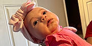 Clara joined the competition — help win amazing prizes! apparel, baby, bow, child, cute, door, face, hand, headband, home, indoor, infant, light, looking_up, person, pink_clothing, portrait, wall, wearing, young_child