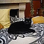 black_cat, cat, bedspread, patterned, yellow_pillow, cushion, indoor, furniture, fireplace, plant, home_decor, resting, pet, cozy, living_room, animal, relaxation, comfort, domestic_cat, feline