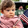 Carter is registered to the contest to win money with this photo: toddler, child, flag, american_flag, hoodie, pink_clothing, outdoor, person, face, blue_eyes, hair, hand, people, background_blur, nature, greenery, casual, patriotic, daylight, portrait