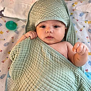 Kai is registered to the contest to win money with this photo: baby, towel, blanket, face, infant, child, cute, hooded_towel, lying_down, indoors, patterned_blanket, soft_texture, wrapped, hand, expression, looking_at_camera, pacifier, toy, colorful, cozy