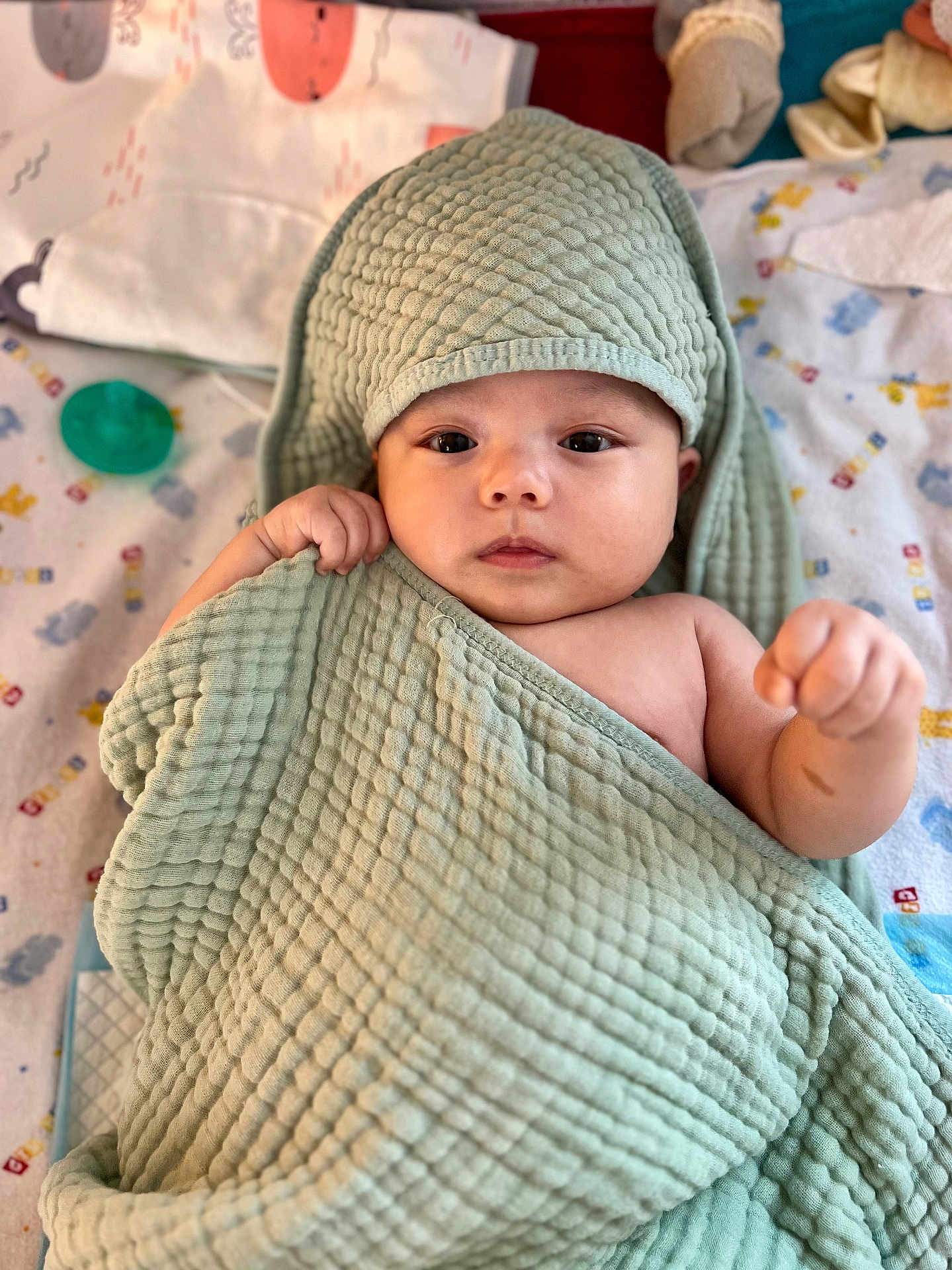 Kai is registered to the contest to win money with this photo: baby, towel, blanket, face, infant, child, cute, hooded_towel, lying_down, indoors, patterned_blanket, soft_texture, wrapped, hand, expression, looking_at_camera, pacifier, toy, colorful, cozy