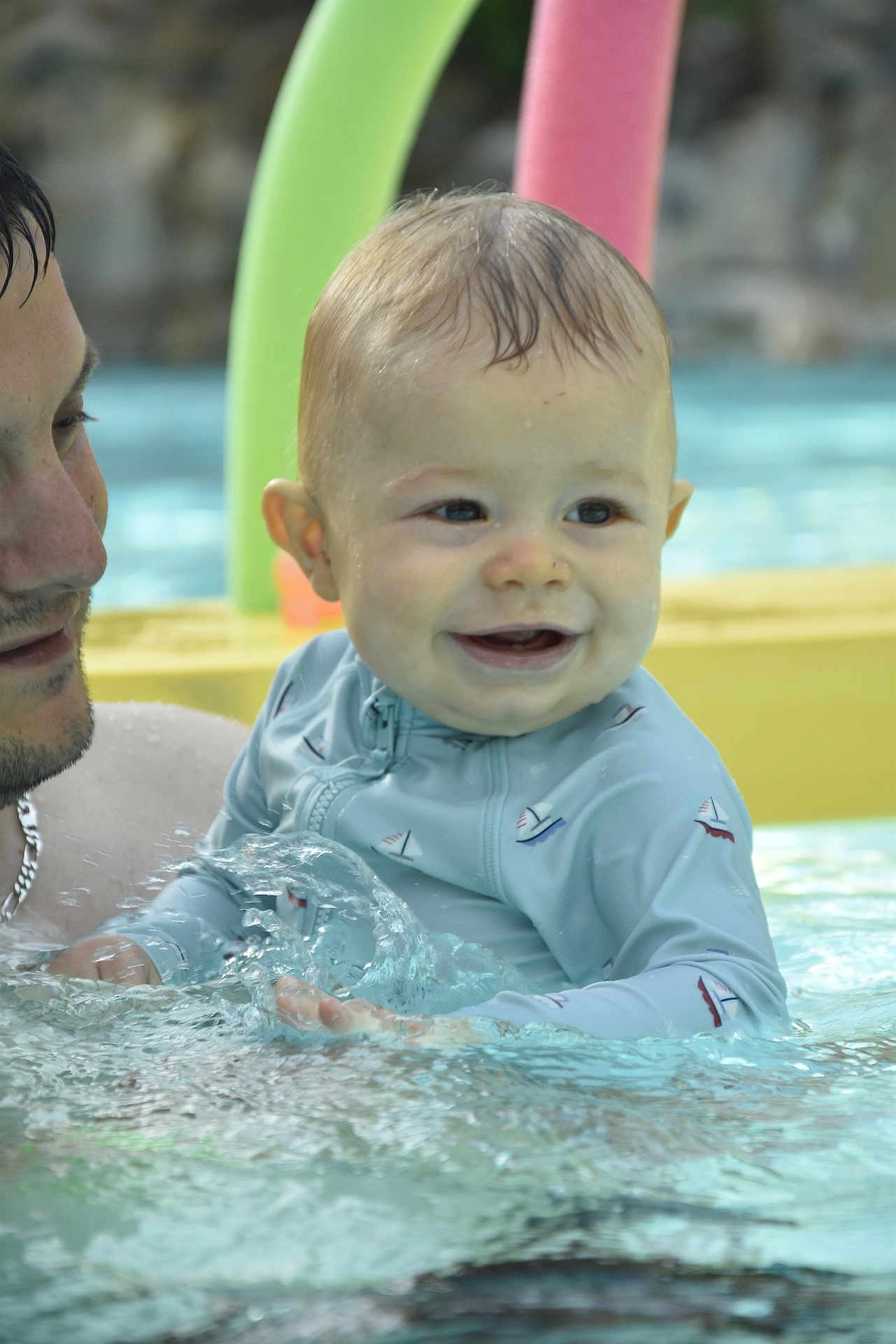 Maël a rejoint le concours — aidez-le/la à gagner de superbes lots ! baby, child, swimming_pool, water, splashing, adult, smiling, swim_shirt, sailboat_pattern, summer, fun, outdoor, playful, parent, support, colorful, toys, happy, face, closeup