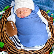 Paxton joined the competition — help win amazing prizes! newborn, baby, sleeping, portrait, basket, woven_basket, blue_wrap, white_hat, hat, football, plush_toy, striped_sock, sock, sports_theme, swaddled, infant, peaceful, indoor, fabric, colorful_decor