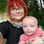Karliah joined the competition — help win amazing prizes! baby, casual_clothing, child, cute, face, family, glasses, greenery, happy, holding, infant, nature, outdoor, parent, person, portrait, red_hair, smile, tattoos, woman